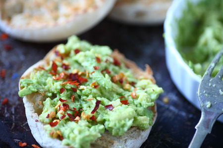 Mashed avocado on English muffin toast rounds sprinkled with red pepper flakes 