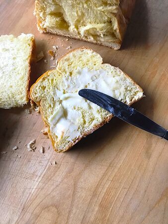 Brioche bread loaf with slices, one buttered, on cutting board