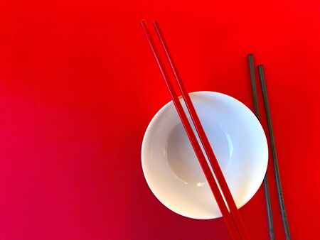 White Chinese bowl with red and black chopsticks on a red backgroundの写真素材