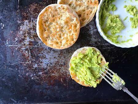 Spreading mashed avocados on toasted English muffins