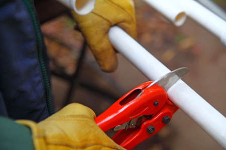 Worker with gloves uses tool to cut a length of PVC pipeの写真素材