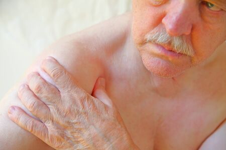 An older man with a hand on an aching shoulder jointの写真素材
