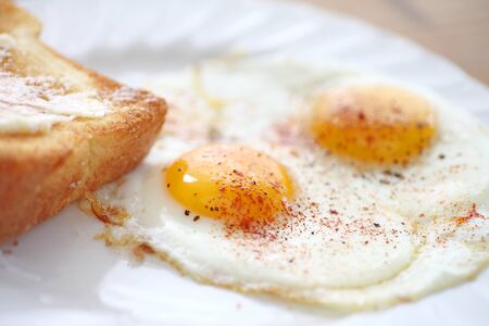 two fried eggs sunny side up, sprinkled with smoked paprika and black pepper, toast alongsideの写真素材