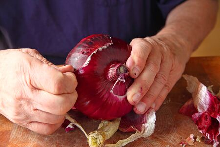 A man peeling the rough outer skin of a large red onionの写真素材