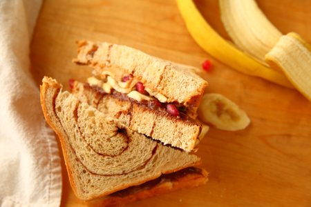 Peanut butter, hazelnut chocolate spread and pomegranate seed sandwich on cinnamon swirl bread on cutting boardの写真素材