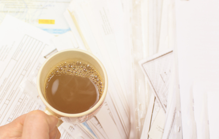 Deadline written on paper and a cup of coffee in hand against a background of scattered papers. Toned.の写真素材