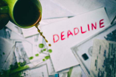 Pouring coffee on the inscription deadline against the background of scattered papers.の写真素材