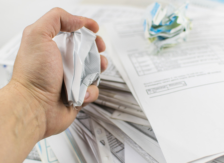 A man's hand holds a crumpled document against a backdrop of scattered papers.の写真素材