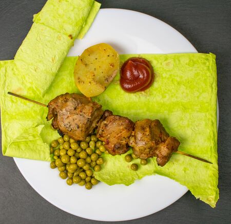 Fried meat on green pita bread with spinach and peas and baked potatoes.の写真素材