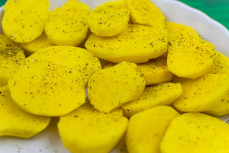 Sliced raw potatoes with spices on a dish for baking.の写真素材