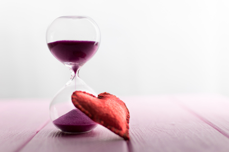 Outgoing love in time. Hourglass and heart on a pink background.の写真素材