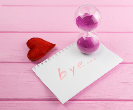 End of love. Hourglass and the word bye on a piece of paper with a heart next to it.