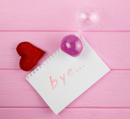 End of love. Hourglass and the word "bye" on a piece of paper with a heart next to it.の写真素材