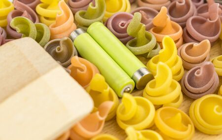 Multicolored pasta and two batteries. The concept of energy in food. on a wooden background.