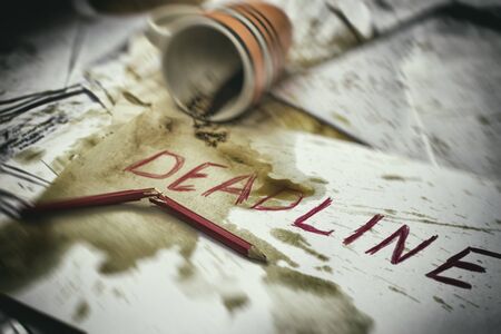 Deadline written on paper in red on the background of spilled coffee and a broken pencil.の写真素材