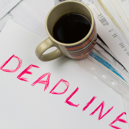 Deadline written on paper and a cup of coffee on scattered papers. Toned.の写真素材