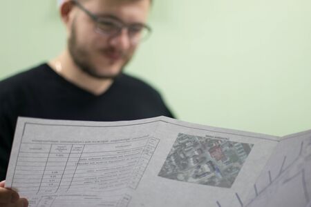 An engineer with glasses with a beard is not in the focus of studying a project on paper.