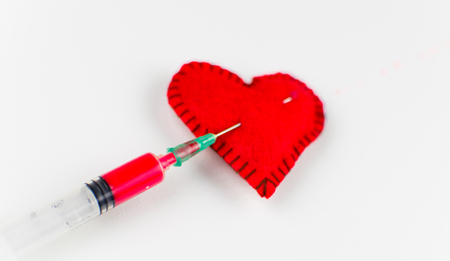An injection of love in the heart. Stitched heart and syringe with red liquid on a white background.の写真素材