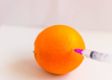 The concept of non-natural products, gmo. Syringe and orange on a white background.の写真素材