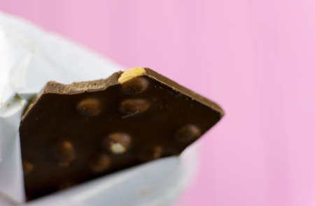 A bitten chocolate bar with nuts on a pink background.の写真素材