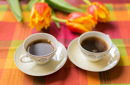 Two small cups of coffee on the saucers on the table with tulips. Meeting for two veterans: May 9 is the day of victory.の写真素材