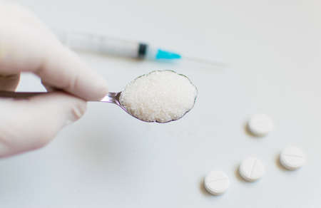 A spoon of sugar, a syringe and pills on a white background. The concept of harm to sugar and the onset of diabetes.の写真素材