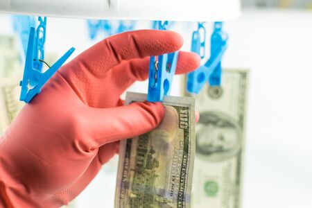 A hand in a rubber glove removes 100 dollars, which hang on the clothespin on a white background.の写真素材
