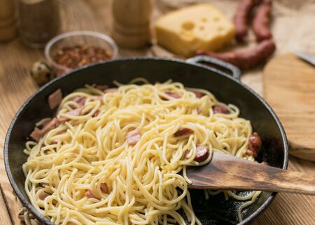 Spaghetti with sausages, cheese and quail eggs in a frying pan.の写真素材