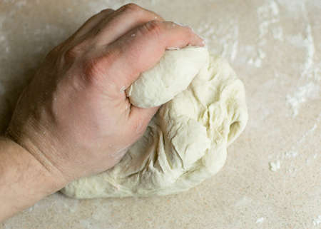 A man's hand kneads a dough.