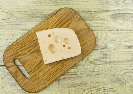 A piece of cheese with large holes on a wooden cutting board.の写真素材