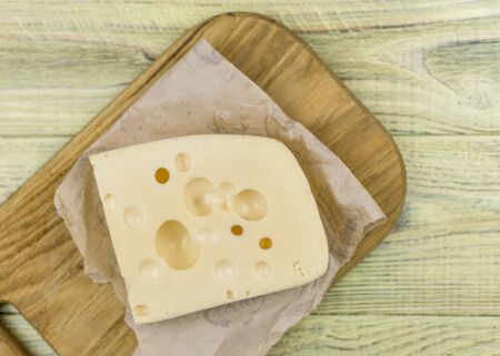 A piece of cheese with large holes on a wooden cutting board.