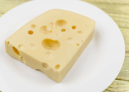 A piece of cheese with holes and a knife for cutting on a white plate.の写真素材