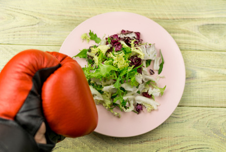 Nutrition for sports, healthy active way of life. Vegetarian salad of fresh vegetables and boxing gloves on a wooden background.の写真素材