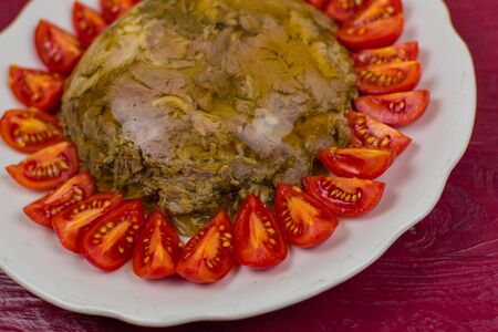 A jellied meat in a round plate decorated with tomatoes on a wooden surface of a color tawny port.の写真素材