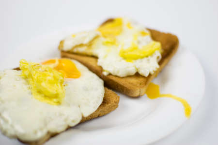 Fried chicken eggs with a burst yolk on toast on a white plate.の写真素材