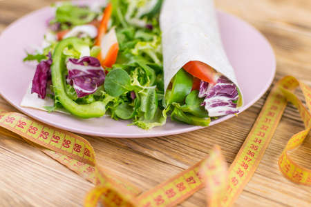 Fitness salad and measuring tape on rustic wooden table. Mixed greens, tomatos,  olive oil and...