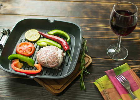 Frying pan with a meatball and vegetables and a glass of wine.