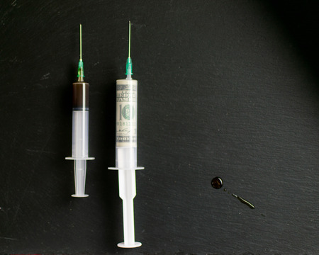 The concept of money and drugs. Money in one syringe and a drug in another on a dark background.の写真素材