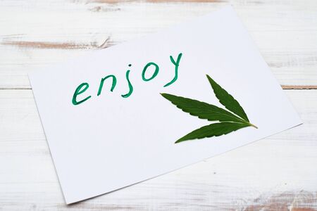 Word enjoy and leaf of marijuana, hemp on a light background. Cannabis as a means of relaxation, enjoyment concept.の写真素材
