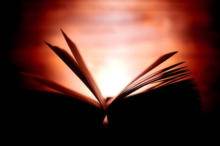 An opened thick book backlit by light on a brown background.の写真素材