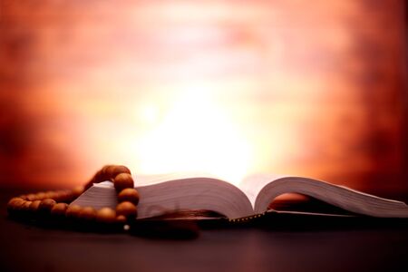 Bible and church rosary on a dark brown background with a radiance behind. Symbol of faith,...