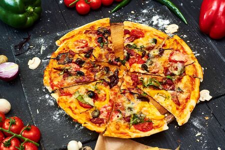 Pizza with mozzarella cheese, tomatoes, mushrooms, peppers, herbs on a dark wooden background.
