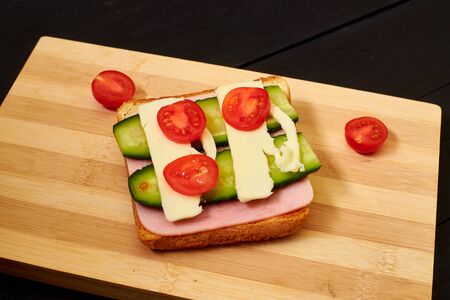 Toast with ham, cheese, cucumber and tomato on a light wooden board.の写真素材