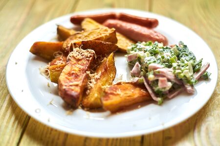 Fried crispy potato with cheese, sausages and salad on a white plate on a wooden background.の写真素材