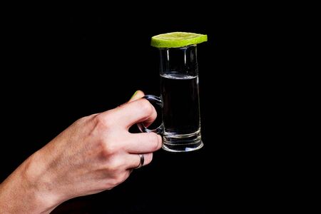 woman holds a glass with tequila, an alcoholic drink on a black background.の写真素材