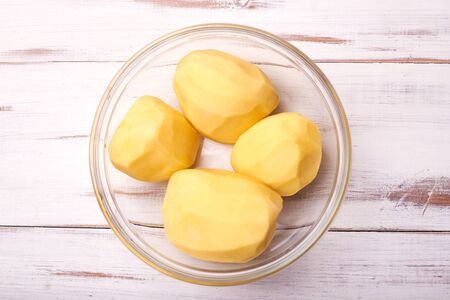 Peeled potato tubers in a plate on a light wooden background. Preparing potatoes for cooking.の写真素材