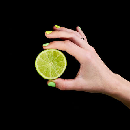 Fresh green lime in a female hand on a black background.の写真素材