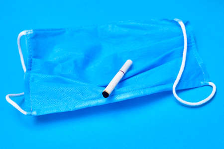 The concept of health and cigarettes. Cigarette in a medical mask on a blue background.の写真素材