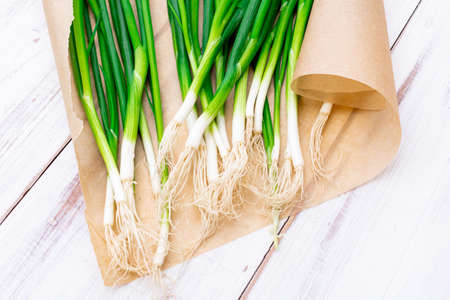 A bunch of green onions on a light wooden background.の写真素材