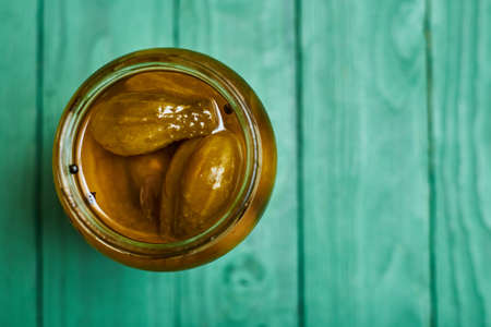 Pickled, canned cucumbers in a jar on a green background.